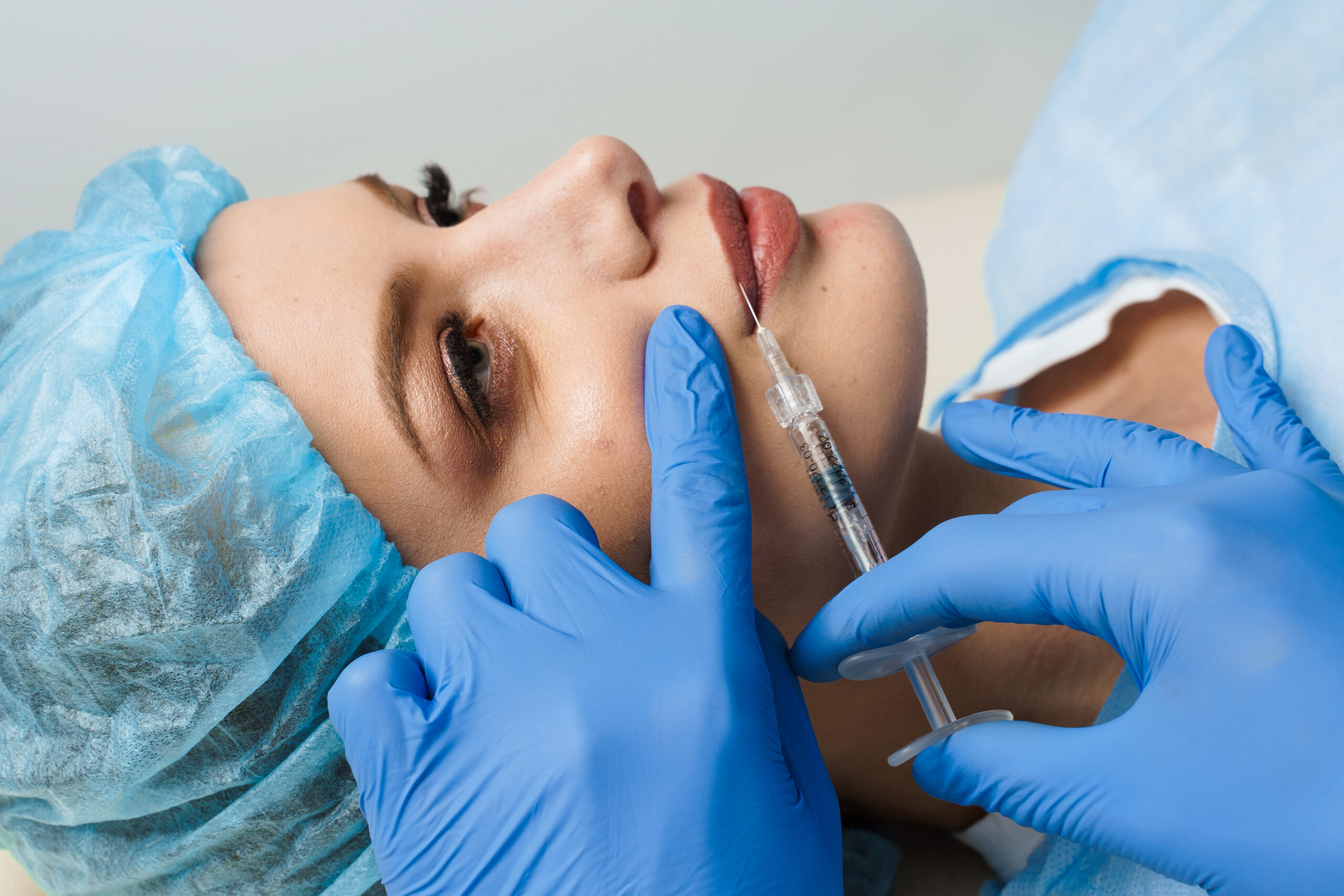 Lips augmentation injections for attractive girl on white background. Plastic surgeon does injection in lip in medical clinic.